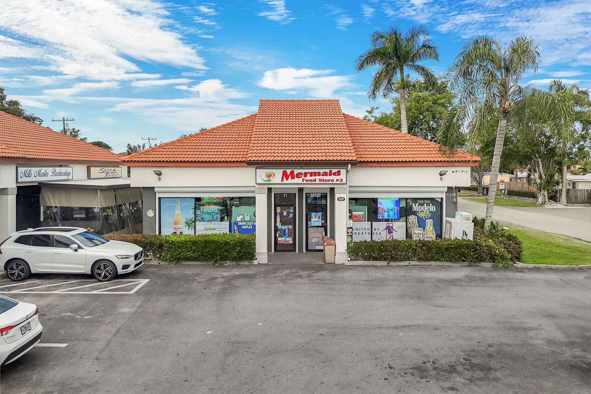 A strip mall with shops, including Mermaid Bait & Tackle, under a blue sky.