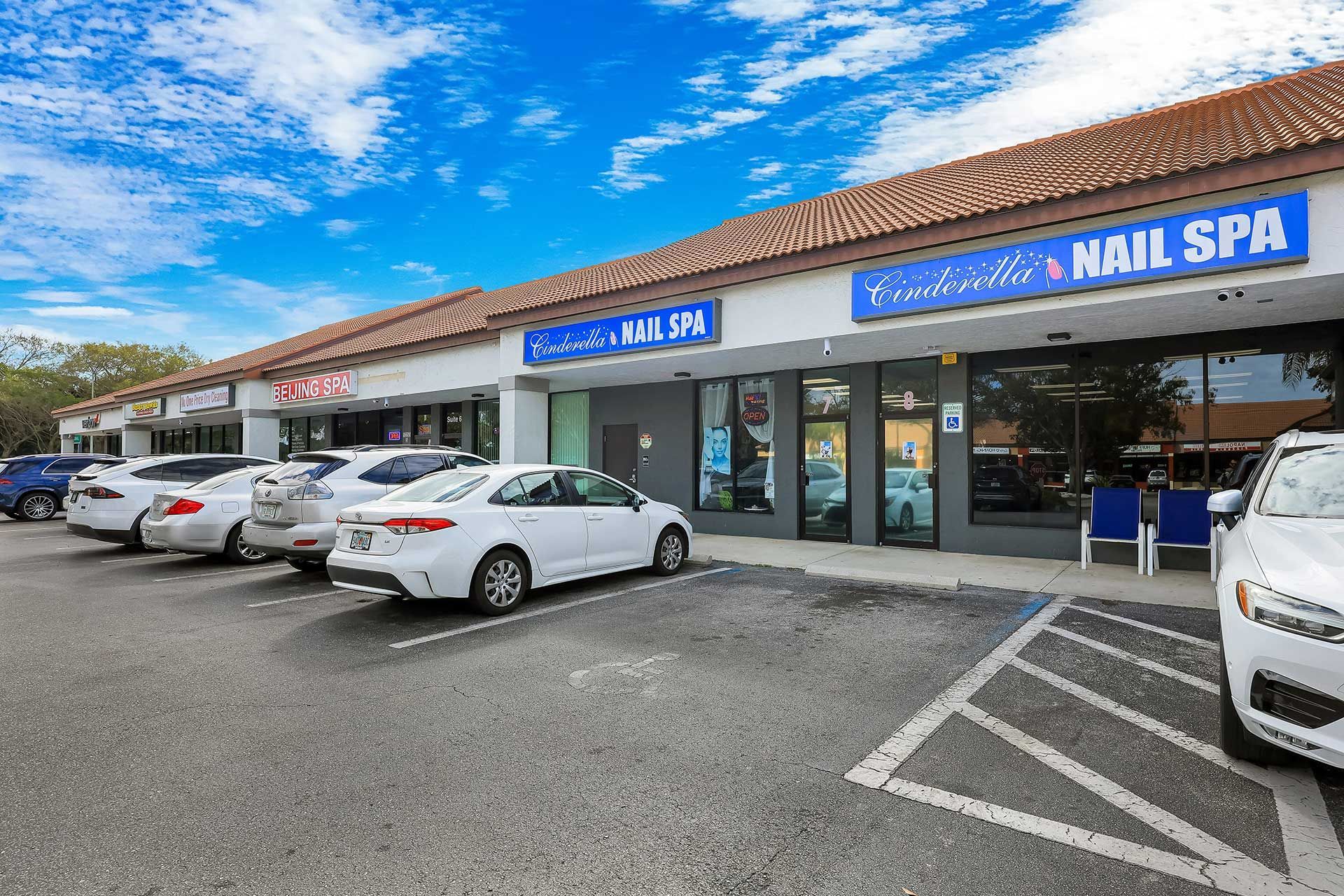 Exterior of a strip mall with Cinderella's Nail Spa and parked cars under a blue sky.