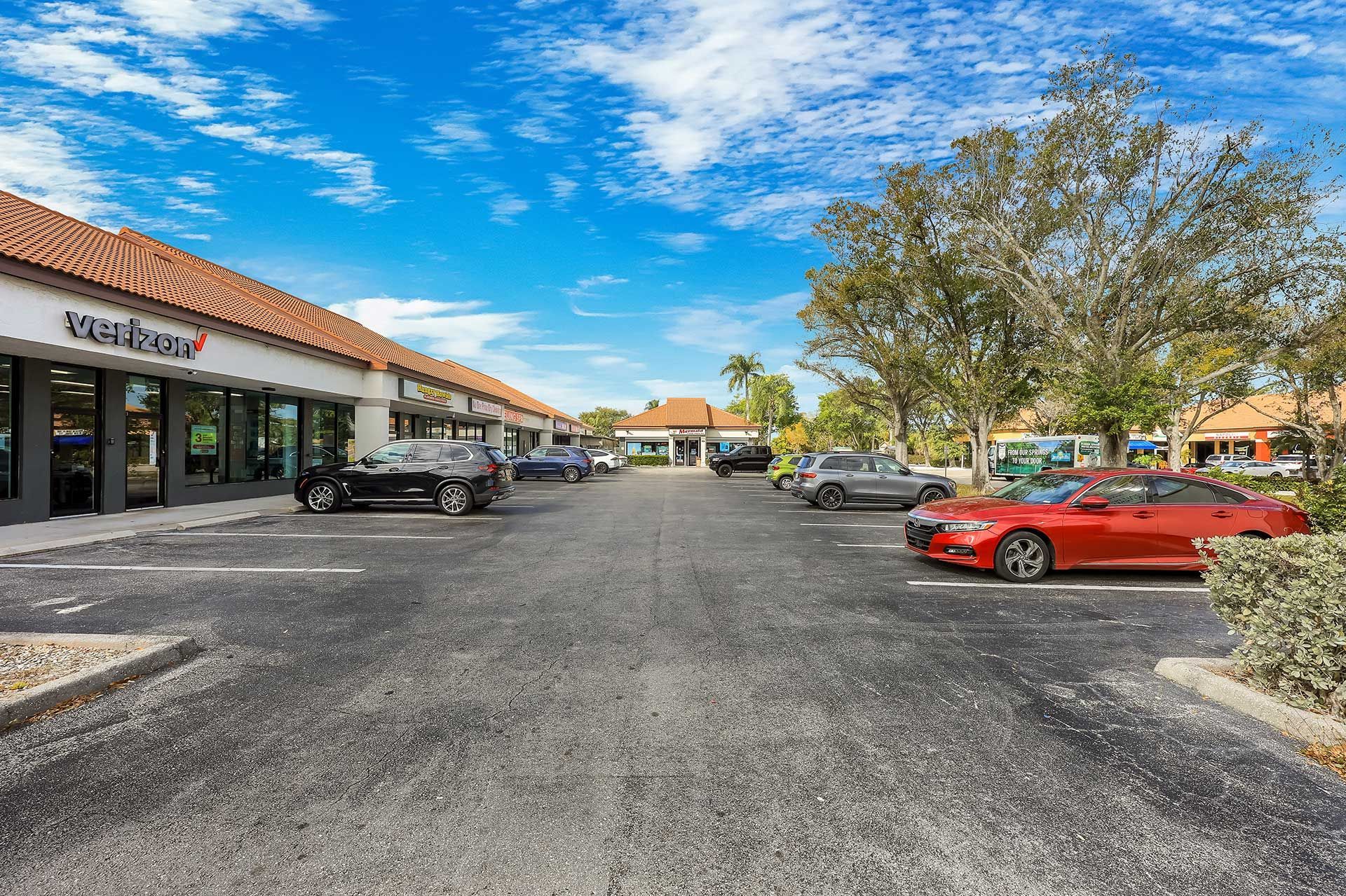 Parking lot in front of a strip mall with cars. Blue sky and some trees.