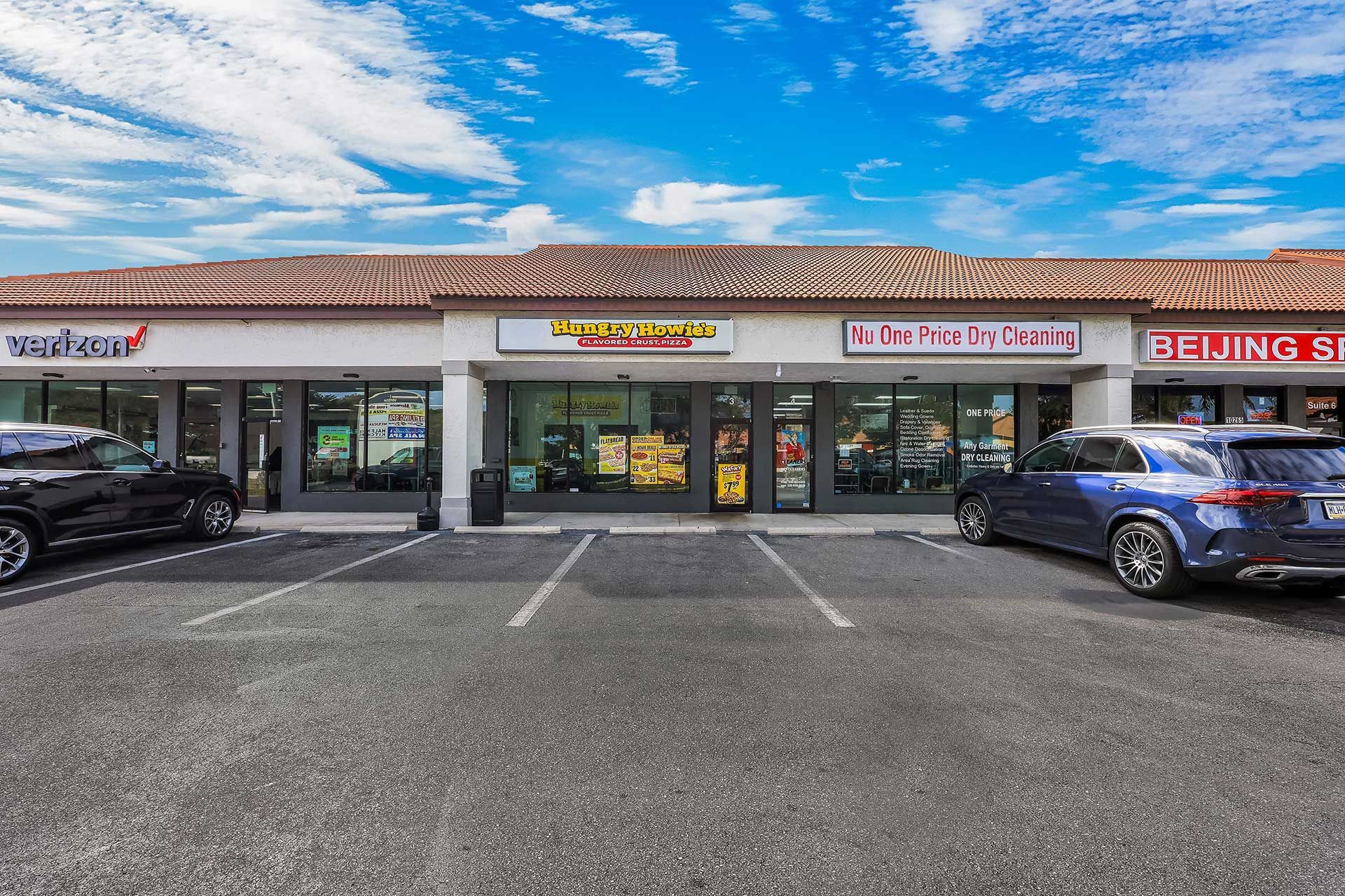 A strip mall with various storefronts, including a restaurant and a clinic, under a bright blue sky.