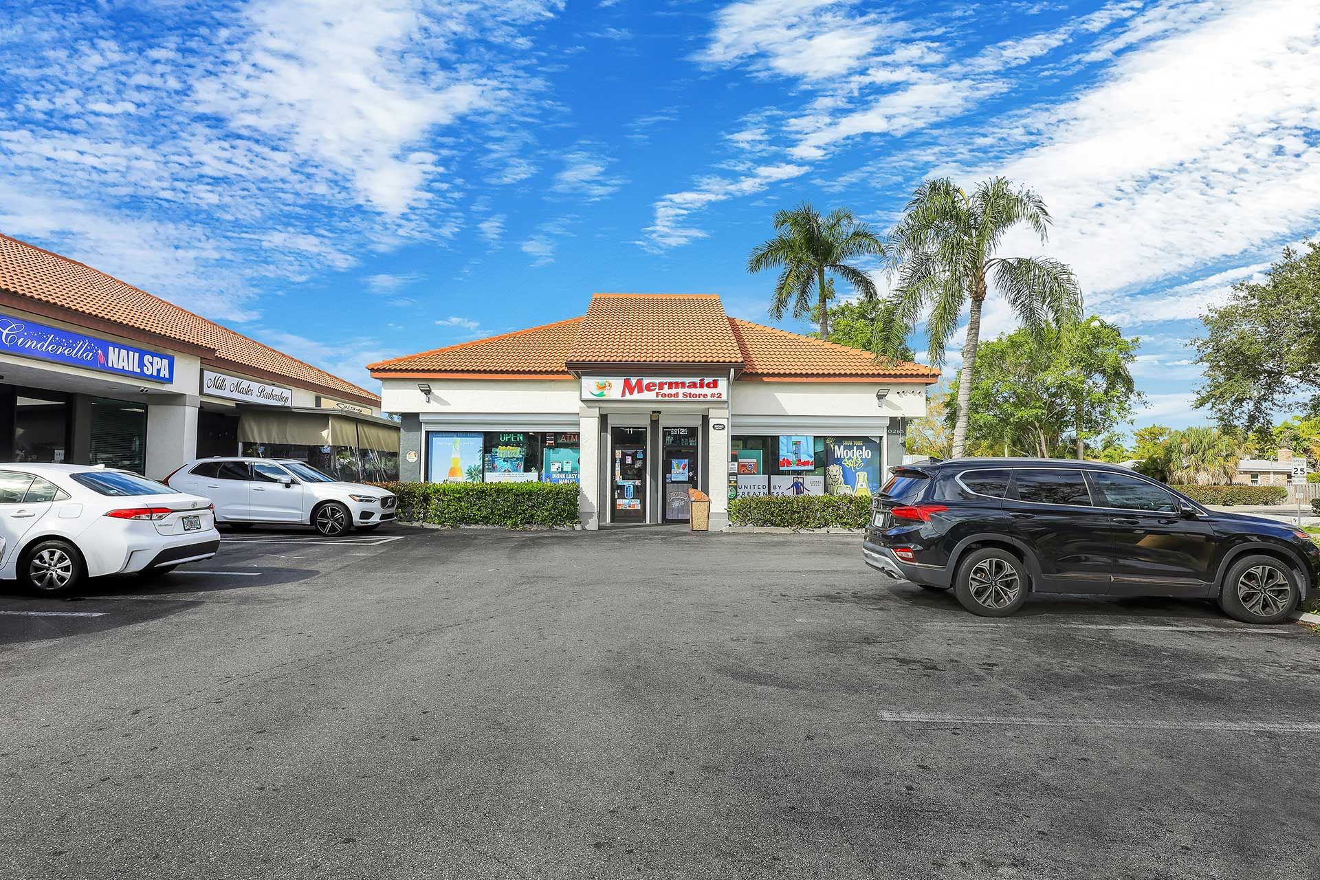 A commercial building with several parked cars. Sunny day with a blue sky and palm trees.