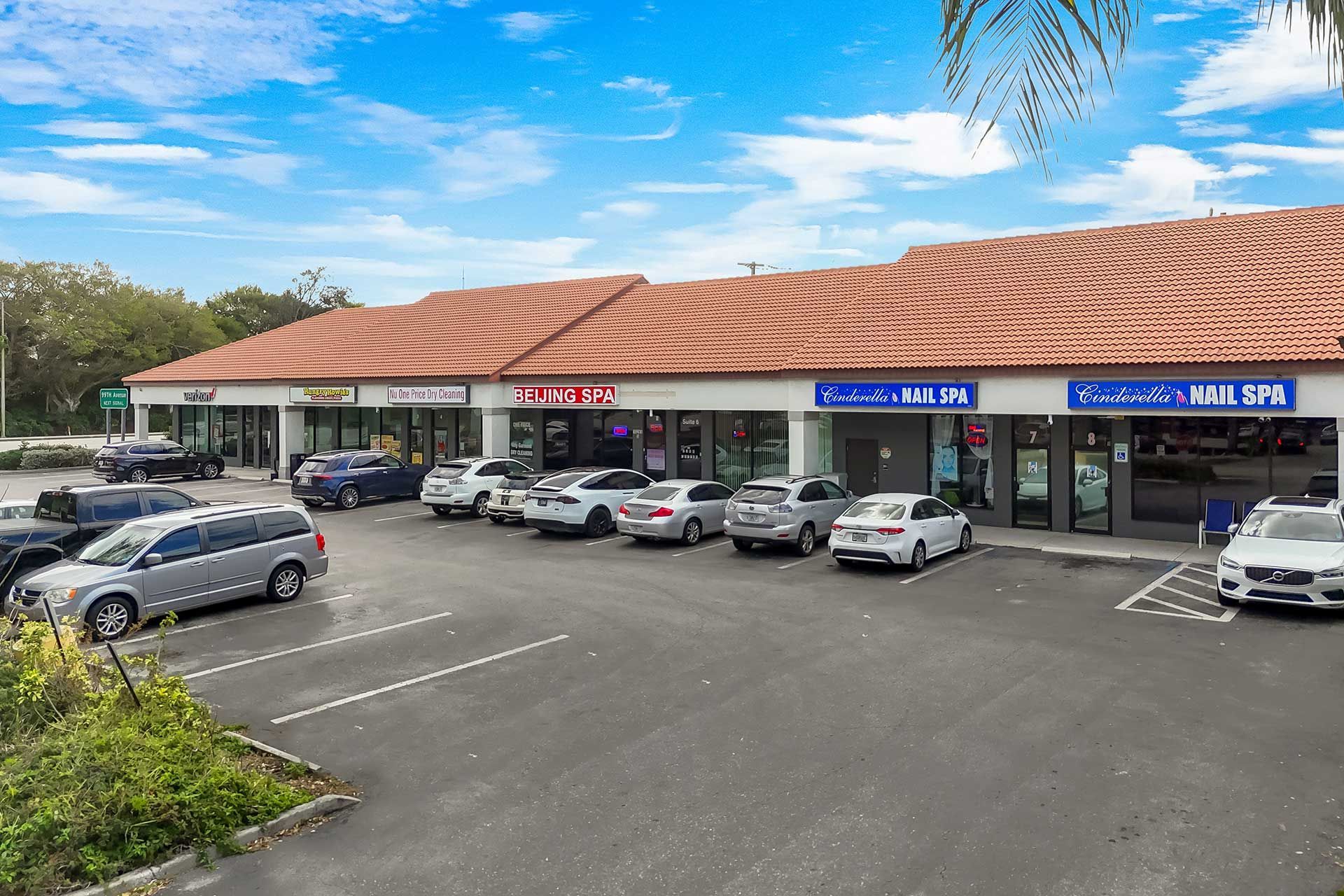 Shops in a strip mall with cars parked in front under a blue sky.
