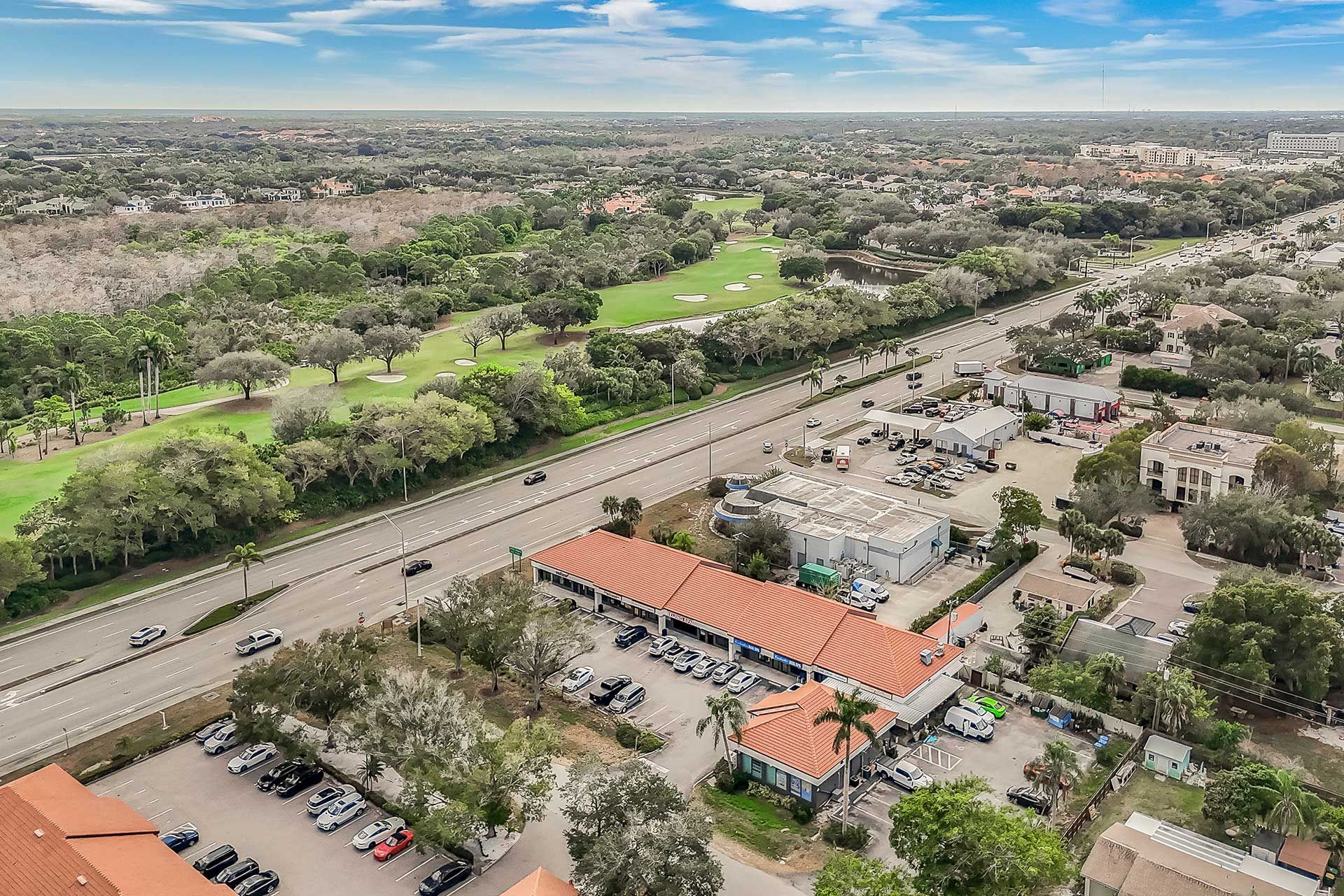 Aerial view of a road lined with trees and buildings, a golf course on the left.