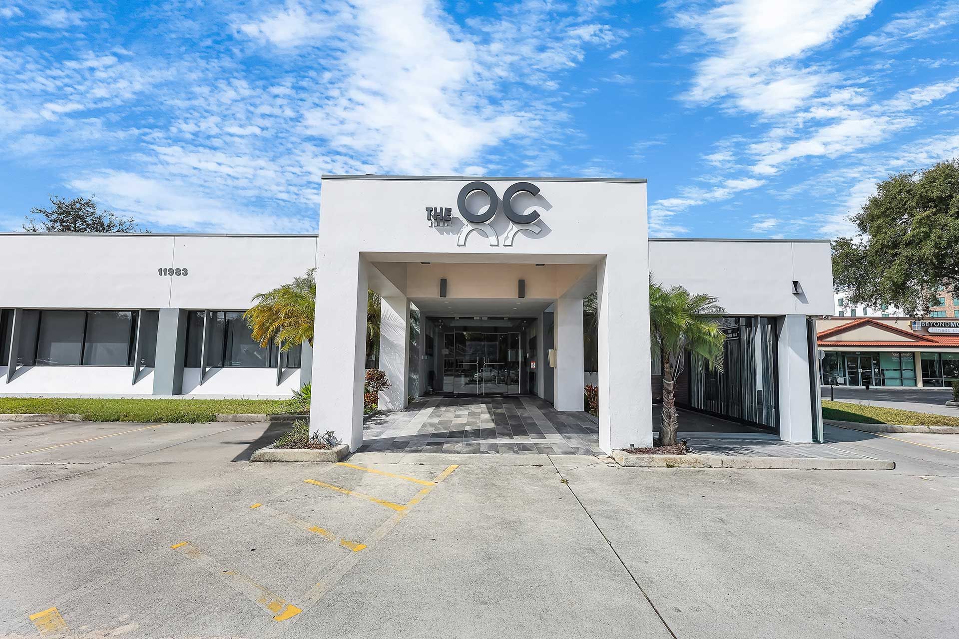 Exterior view of a white commercial building with THE OC signage under a blue sky.
