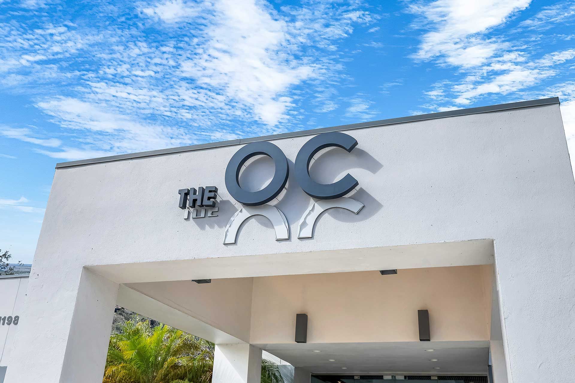 The OC sign above a white entryway with a blue sky background.