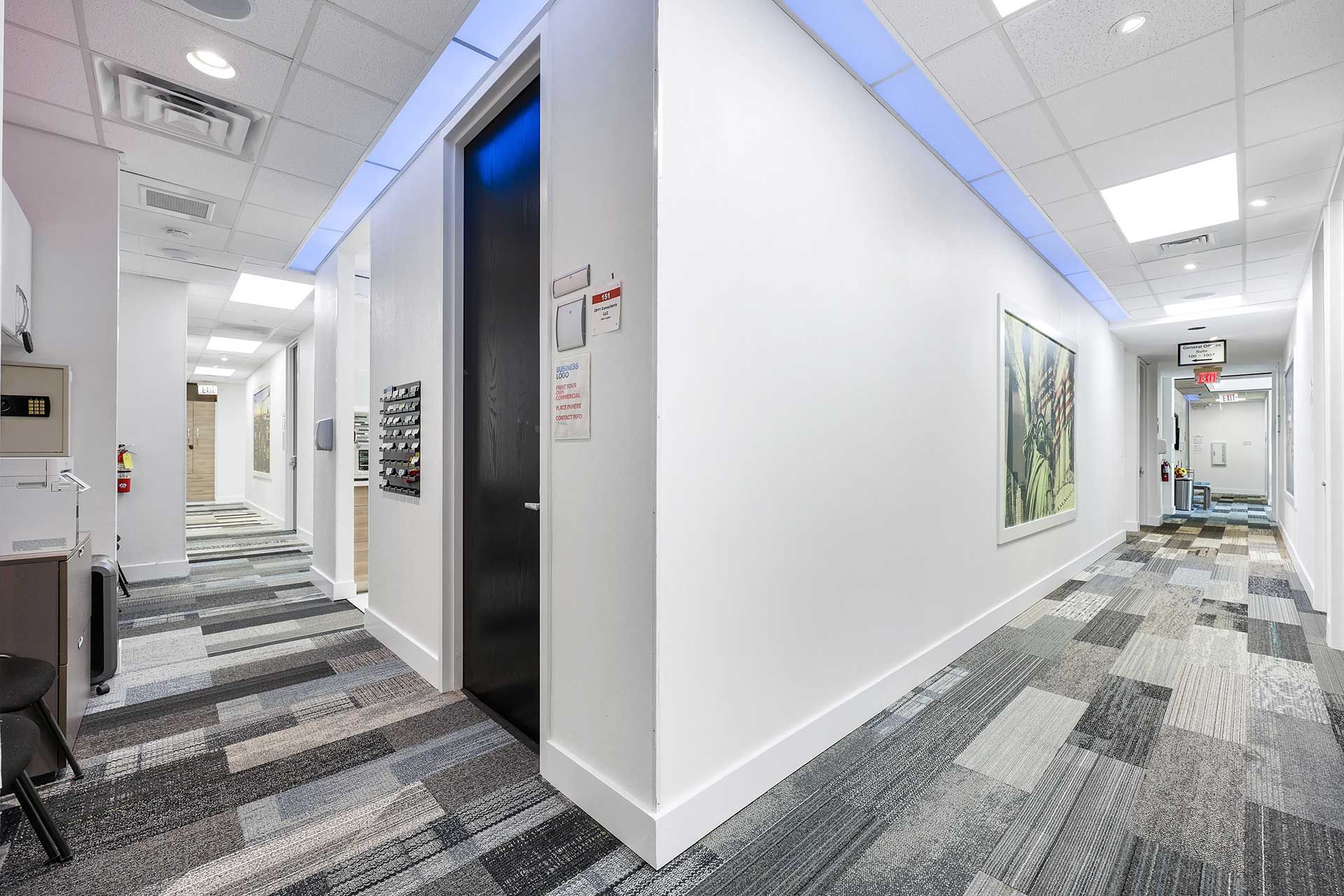 Hallway with colorful patterned carpet, white walls, black door, and artwork.