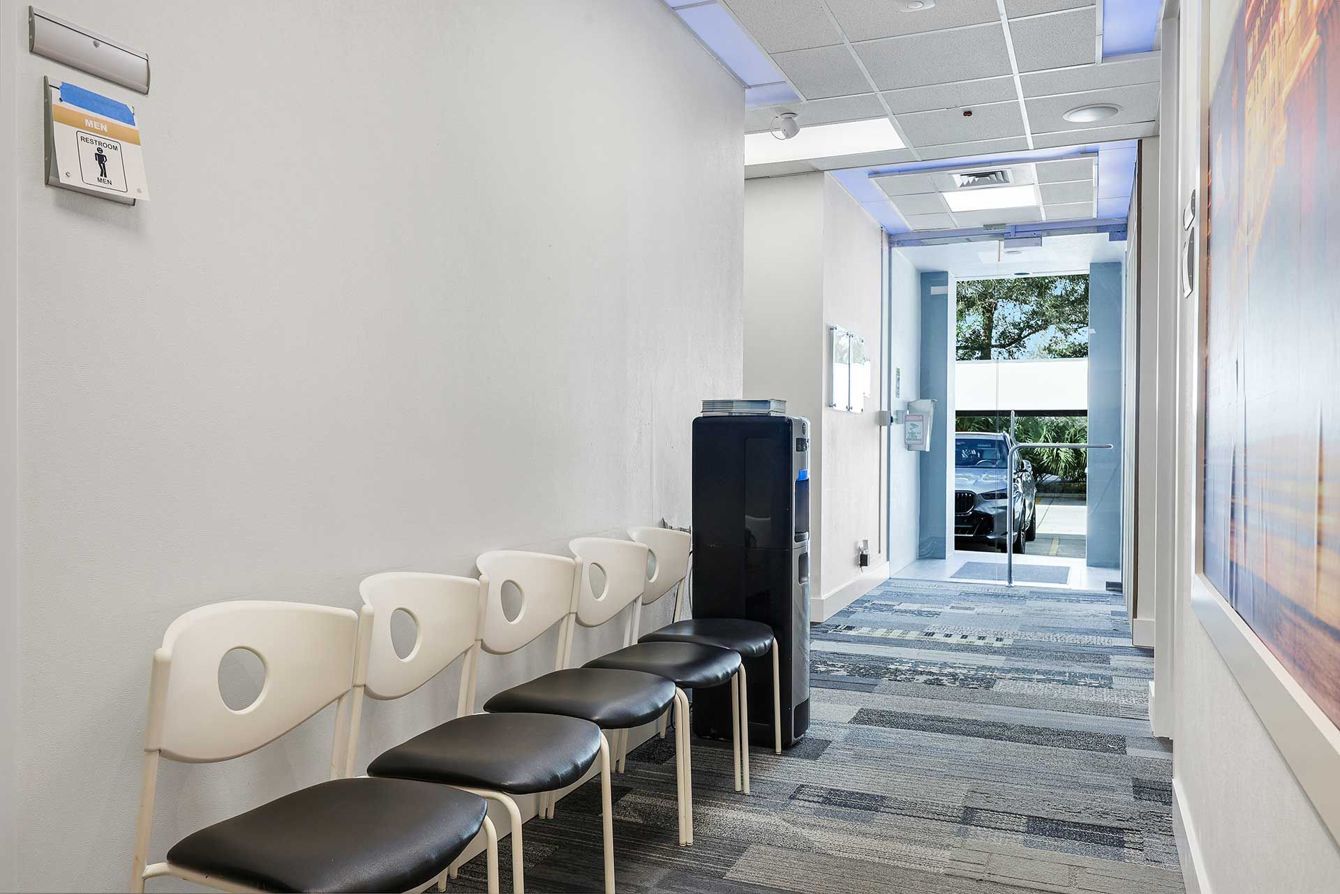 Long, narrow hallway in medical office with chairs, water cooler, and exit to exterior.
