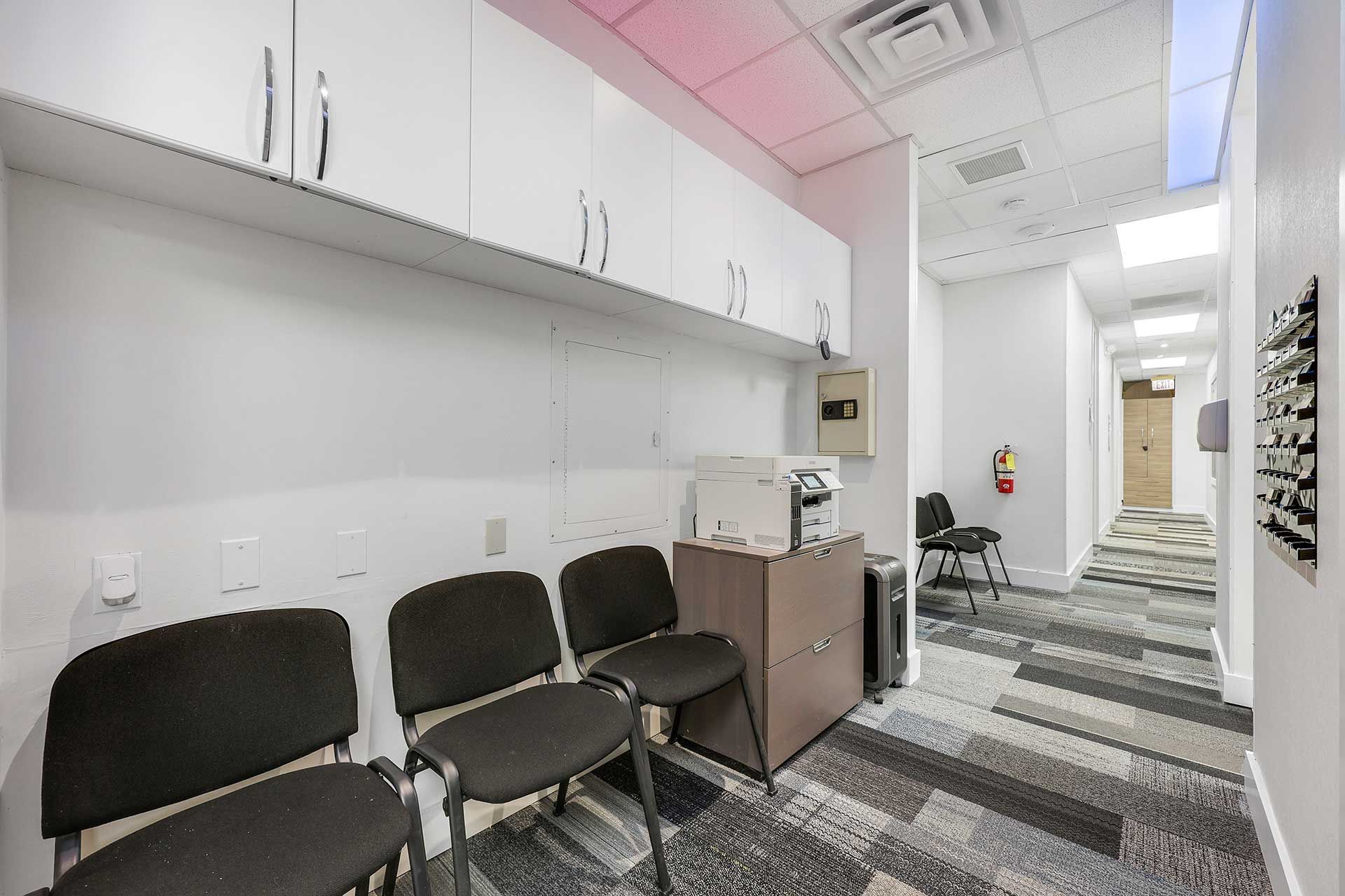 Waiting room with black chairs, cabinets, and a hallway with patterned carpet.