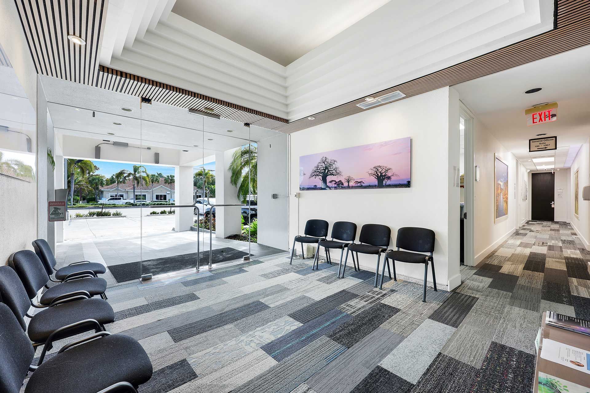 Waiting room with black chairs, glass door, artwork, and patterned carpet.