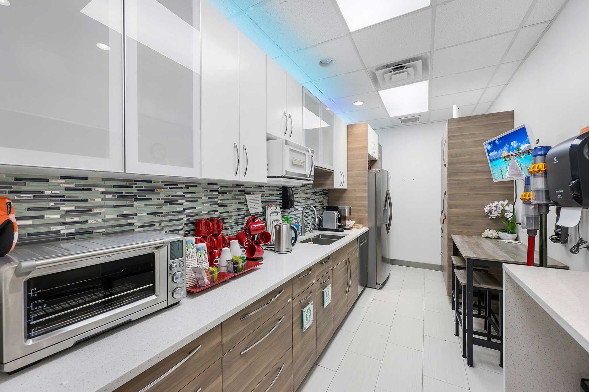 Modern office kitchen with white cabinets, stainless steel appliances, and a small dining area.