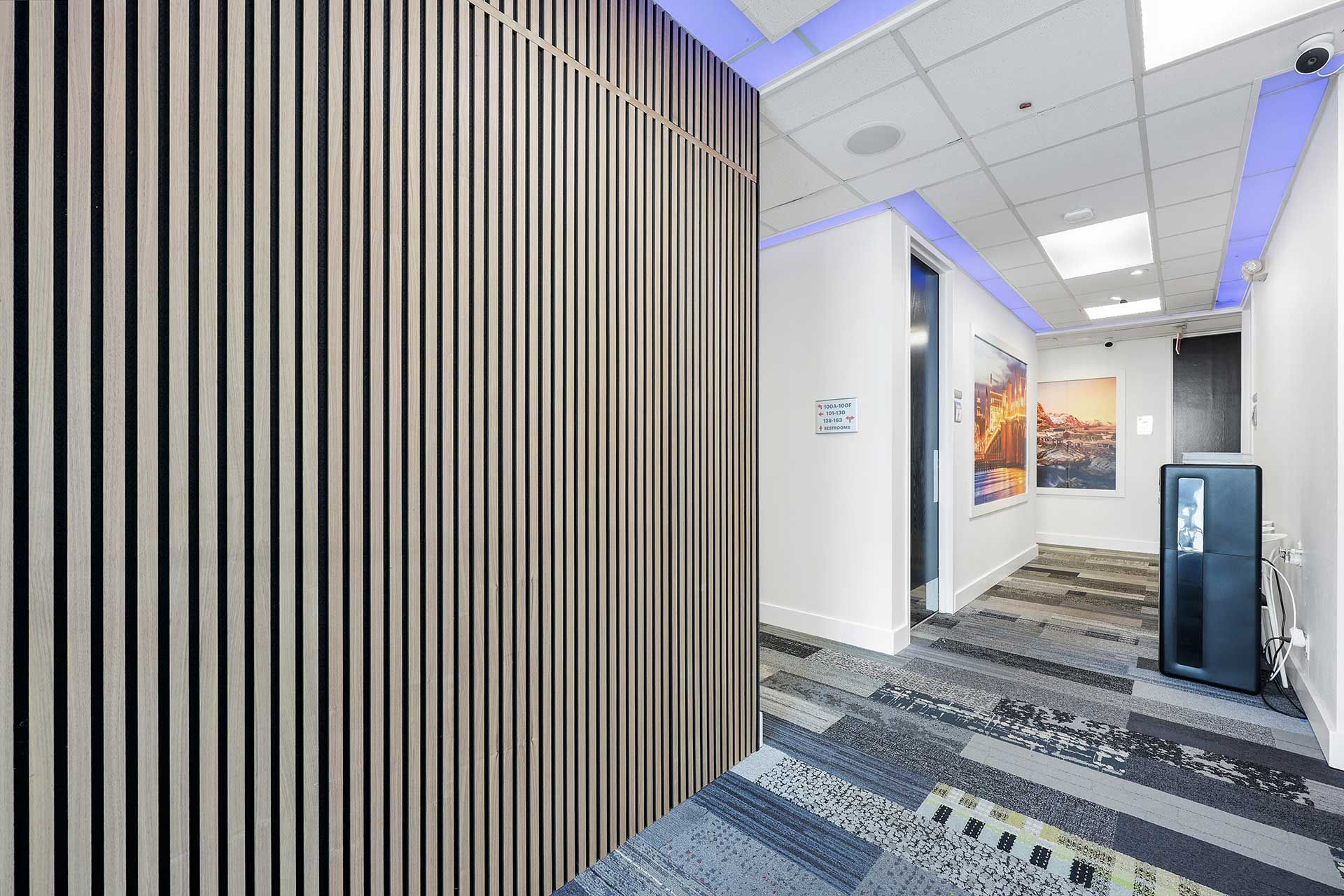 Hallway with vertical wood paneling, patterned carpet, and artwork on the walls.