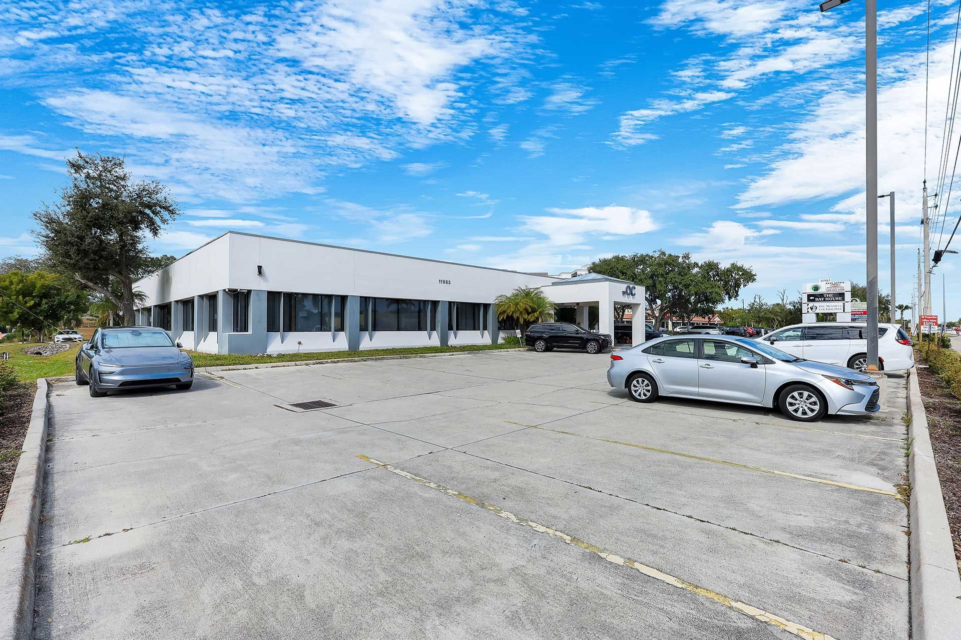 Building with a parking lot and several parked cars under a bright blue sky.