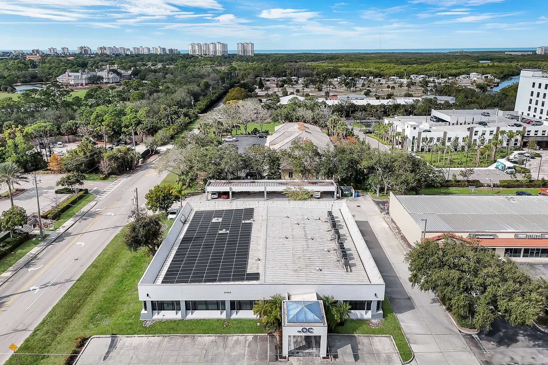 Aerial view of a commercial building with a partially removed roof. Green surroundings and a city skyline are visible.