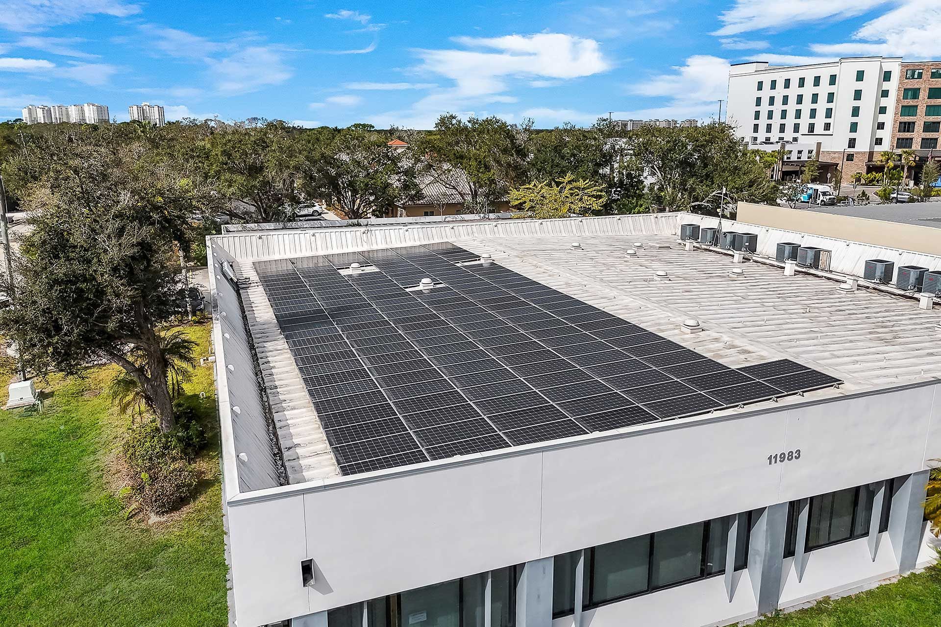 Solar panels on a white commercial building rooftop under a bright blue sky.