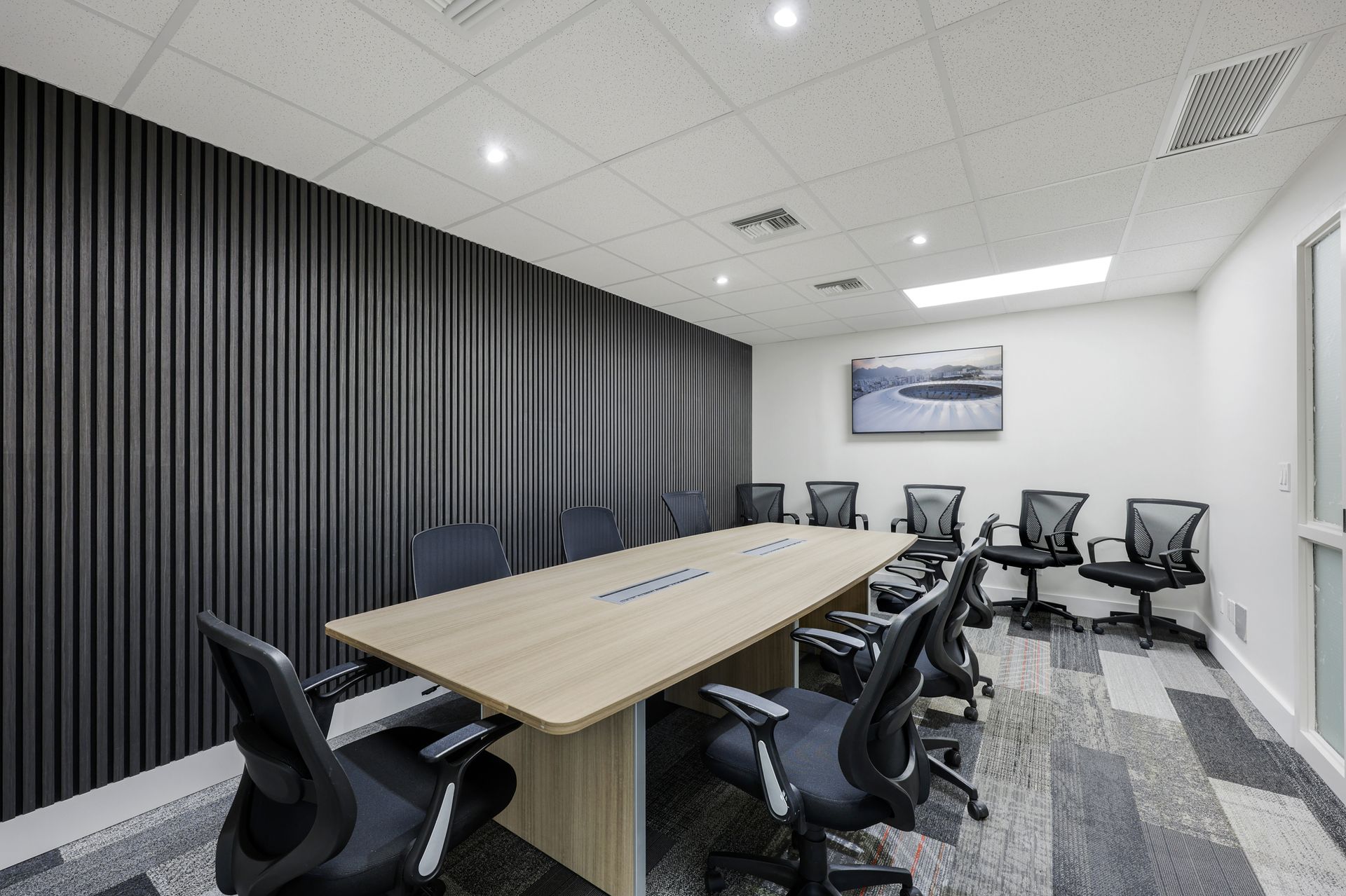 Conference room with long table, black chairs, dark accent wall, and patterned carpet.