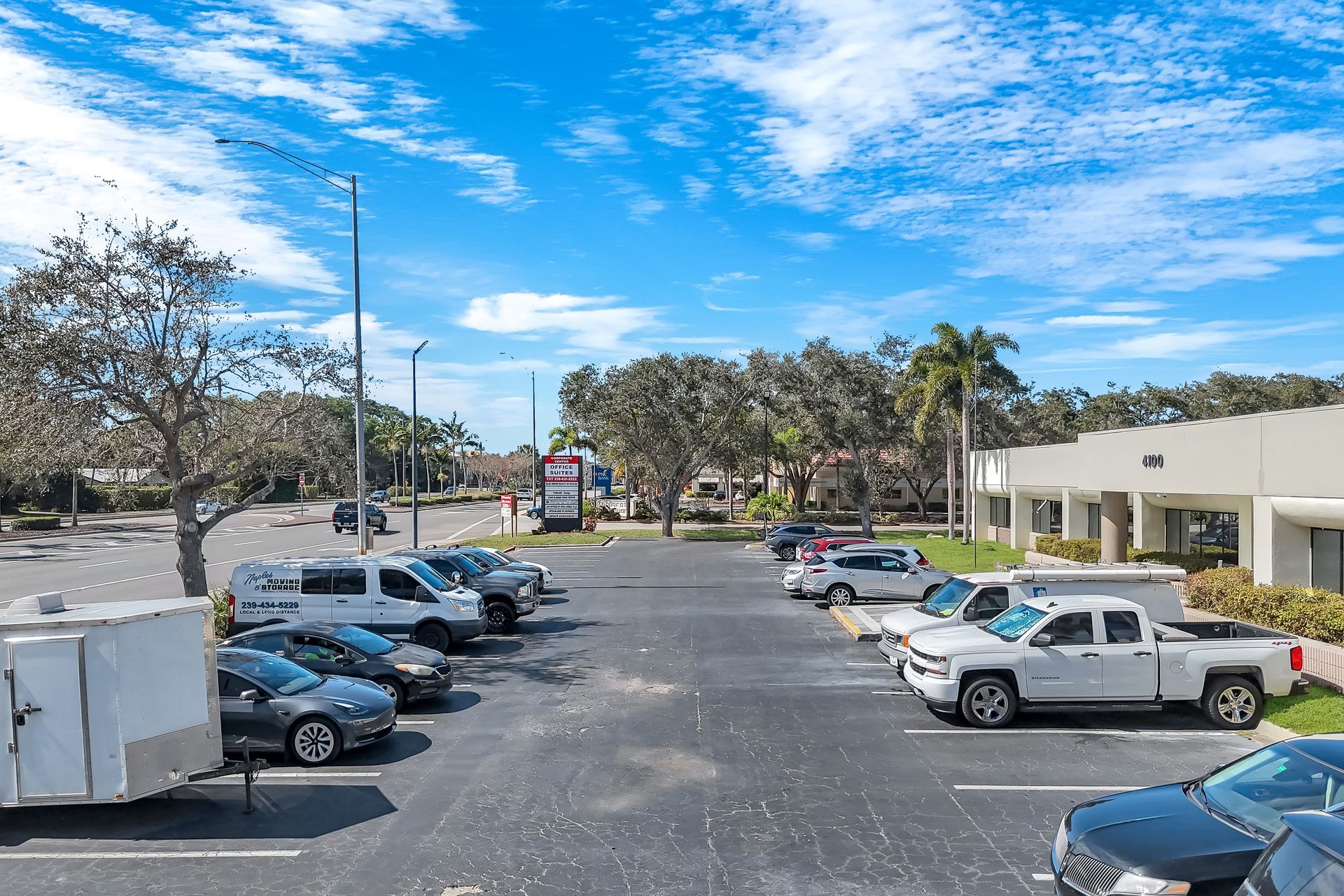 Parking lot with cars, vans, and trucks under a bright blue sky with trees.