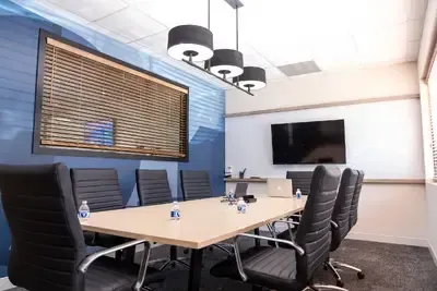Conference room with long table, black chairs, TV, and blue accent wall.
