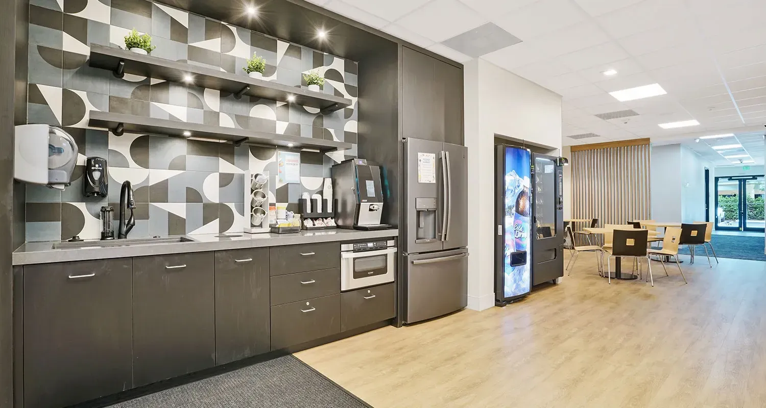 Office break room with kitchenette, shelves, and vending machines.