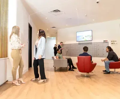 People in an apartment lobby with mailboxes, a TV, and seating. Two women stand talking.