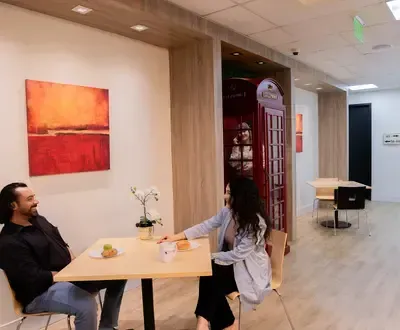 Man and woman sit at a table, smiling. A red phone booth and artwork adorn a brightly-lit room.