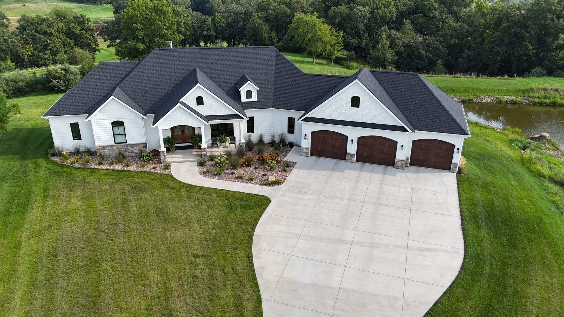 An aerial view of a white, single-story house with a black roof, three-car garage, and a curved concrete driveway.