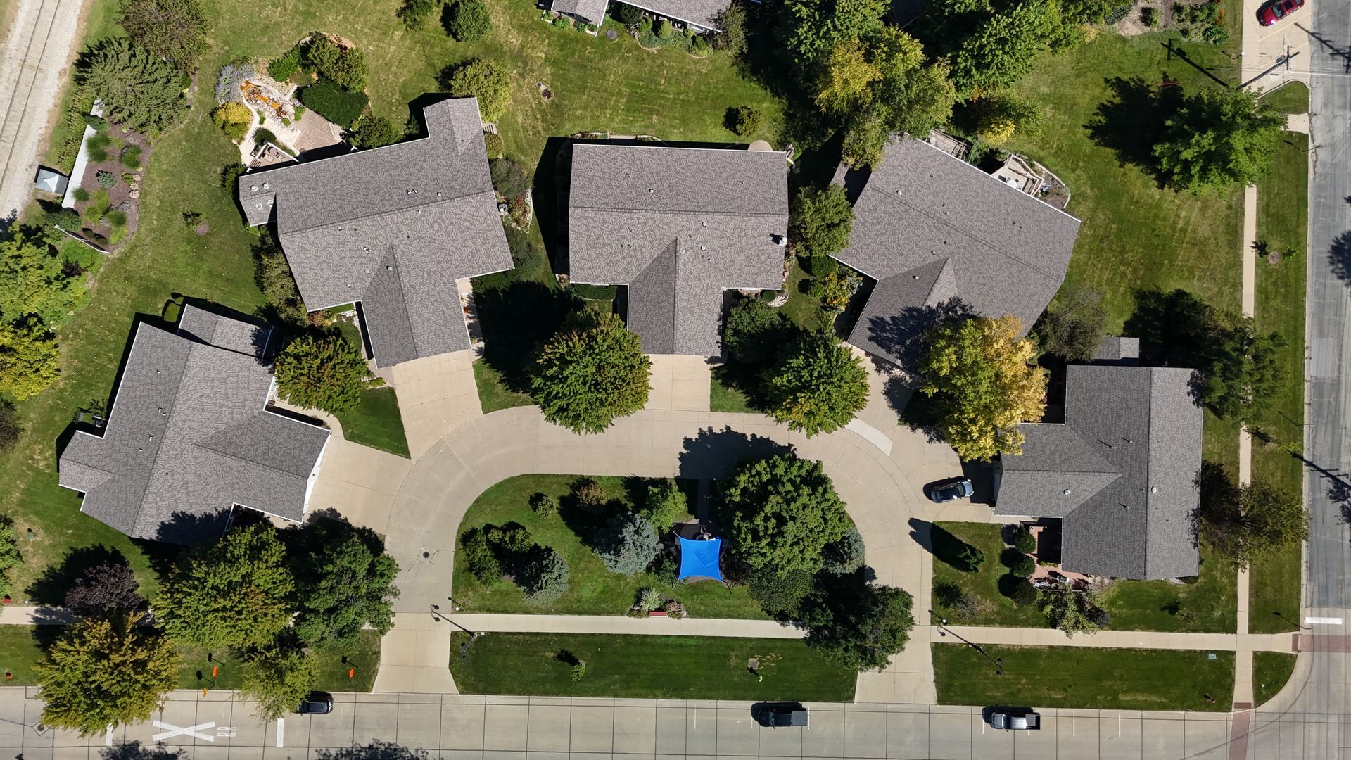 Aerial view of a suburban cul-de-sac with five houses arranged around a curved driveway and central green space.