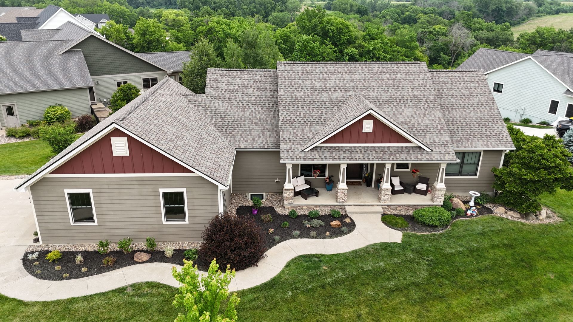 An elevated view of a gray house with a red-accented gable, stone porch columns, and a curved front walkway.
