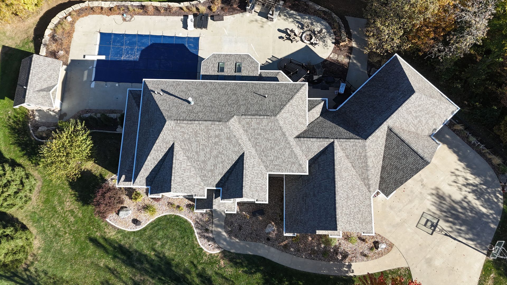 Aerial view of a house with a gray shingled roof, a backyard swimming pool, and a circular concrete driveway.