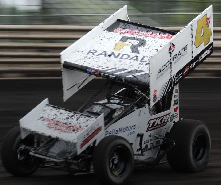 A white number 4 sprint car with large top wings and sponsor decals racing on a dirt track.