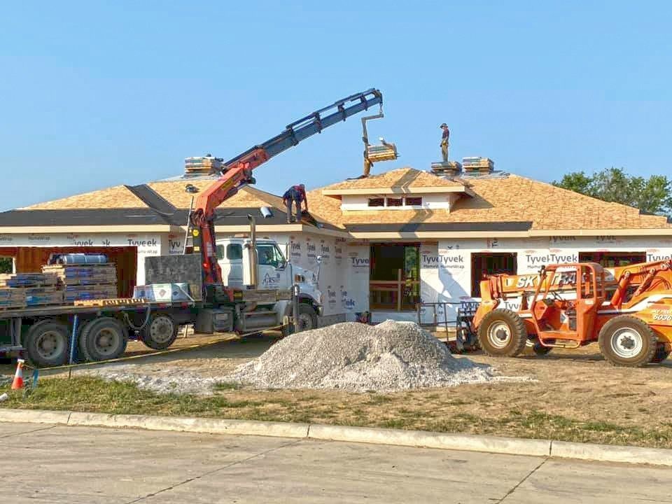 Construction workers on a roof, assisted by a crane truck and a telehandler at a house building site.