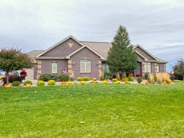 A single-story brick house with a brown roof and evergreen tree, surrounded by a green lawn and autumn landscaping.