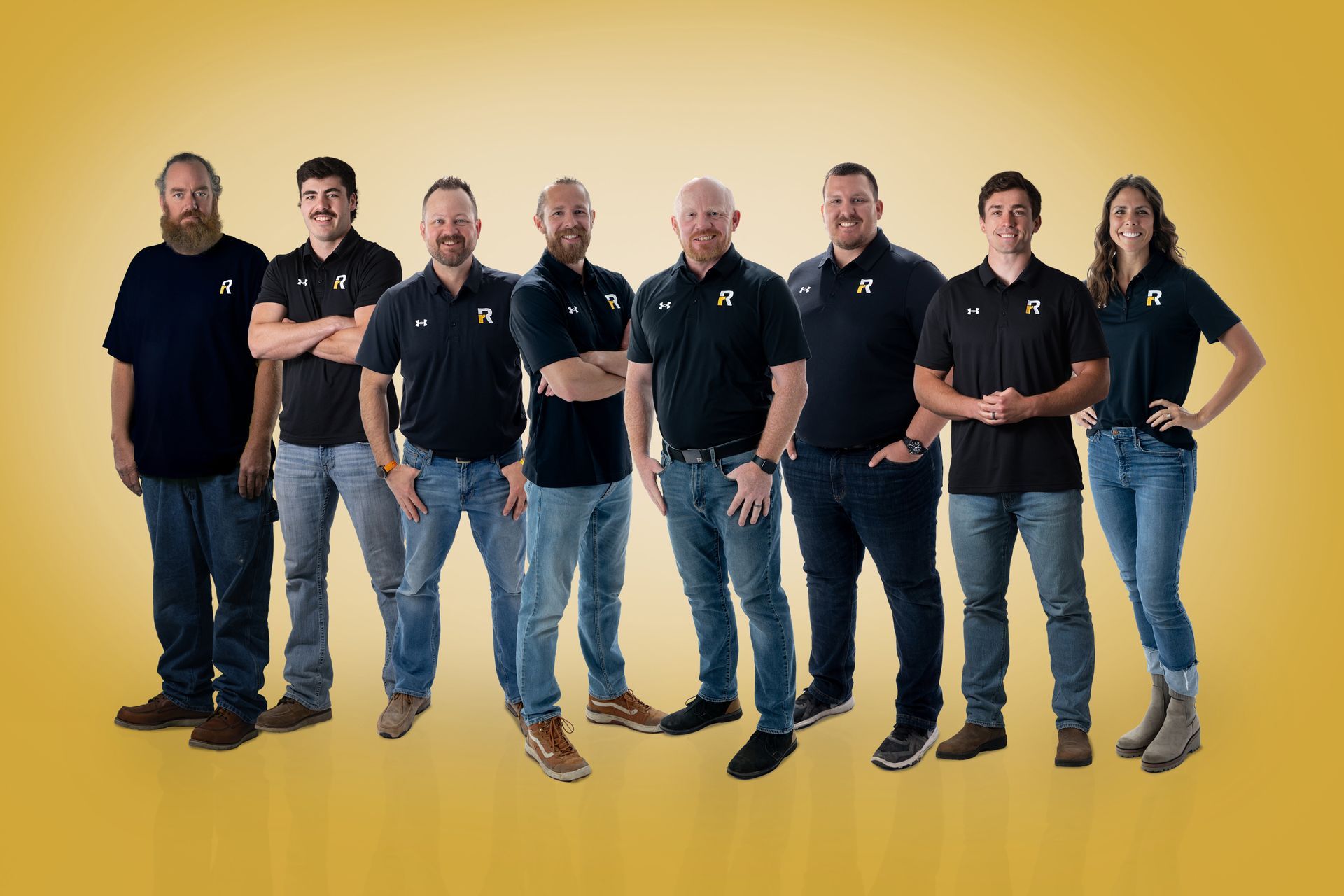 Eight people in black shirts and jeans standing together against a yellow background.