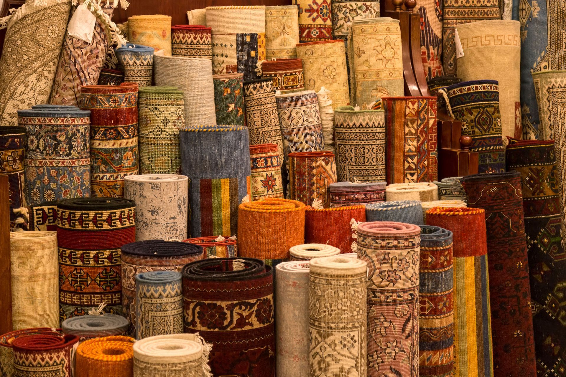Rolled carpets of various colors and patterns stacked for sale.