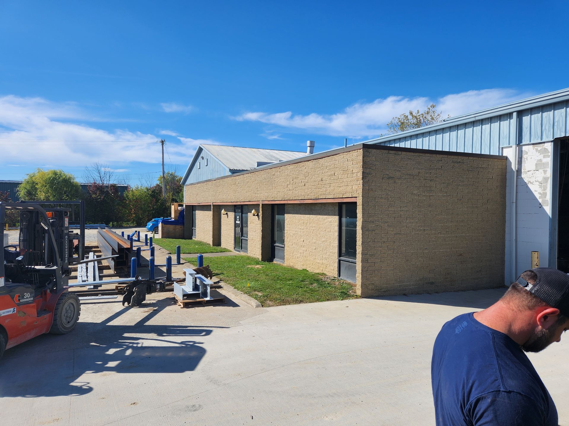 A man is standing in front of a building with a forklift in the background.