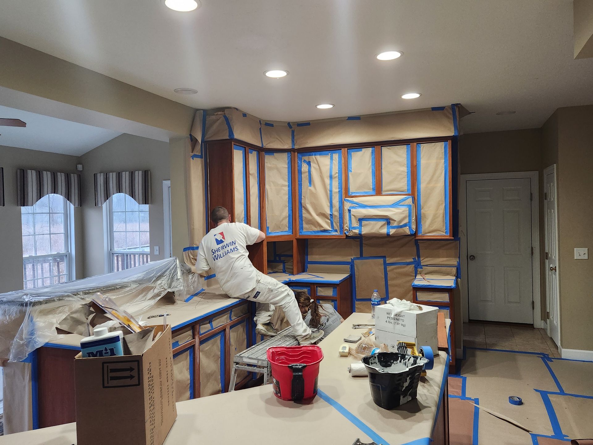 A man is painting a kitchen with blue tape.