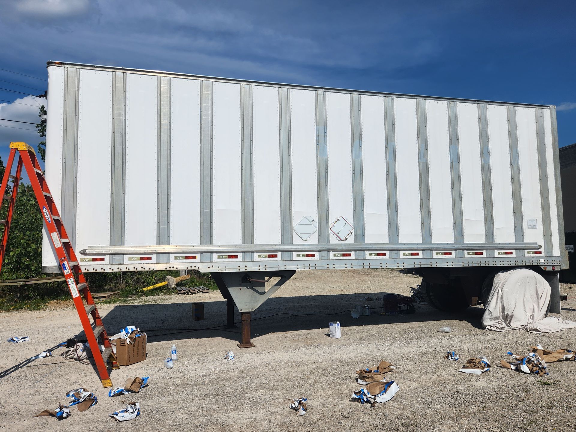 A white trailer is sitting in a gravel lot next to a ladder.