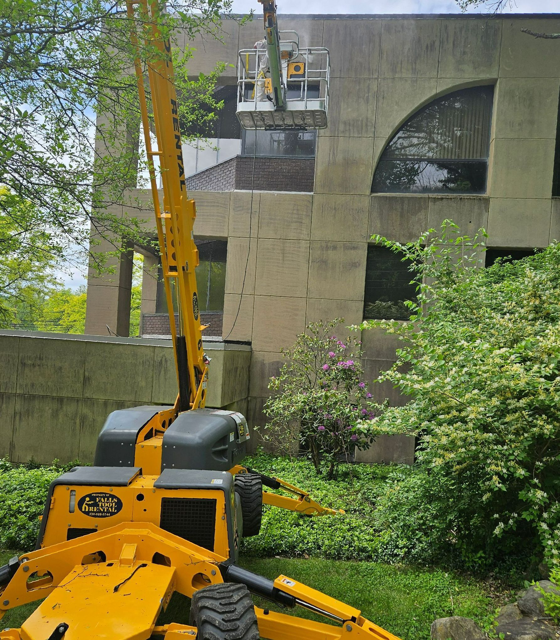 A yellow tractor is cutting a tree in front of a building