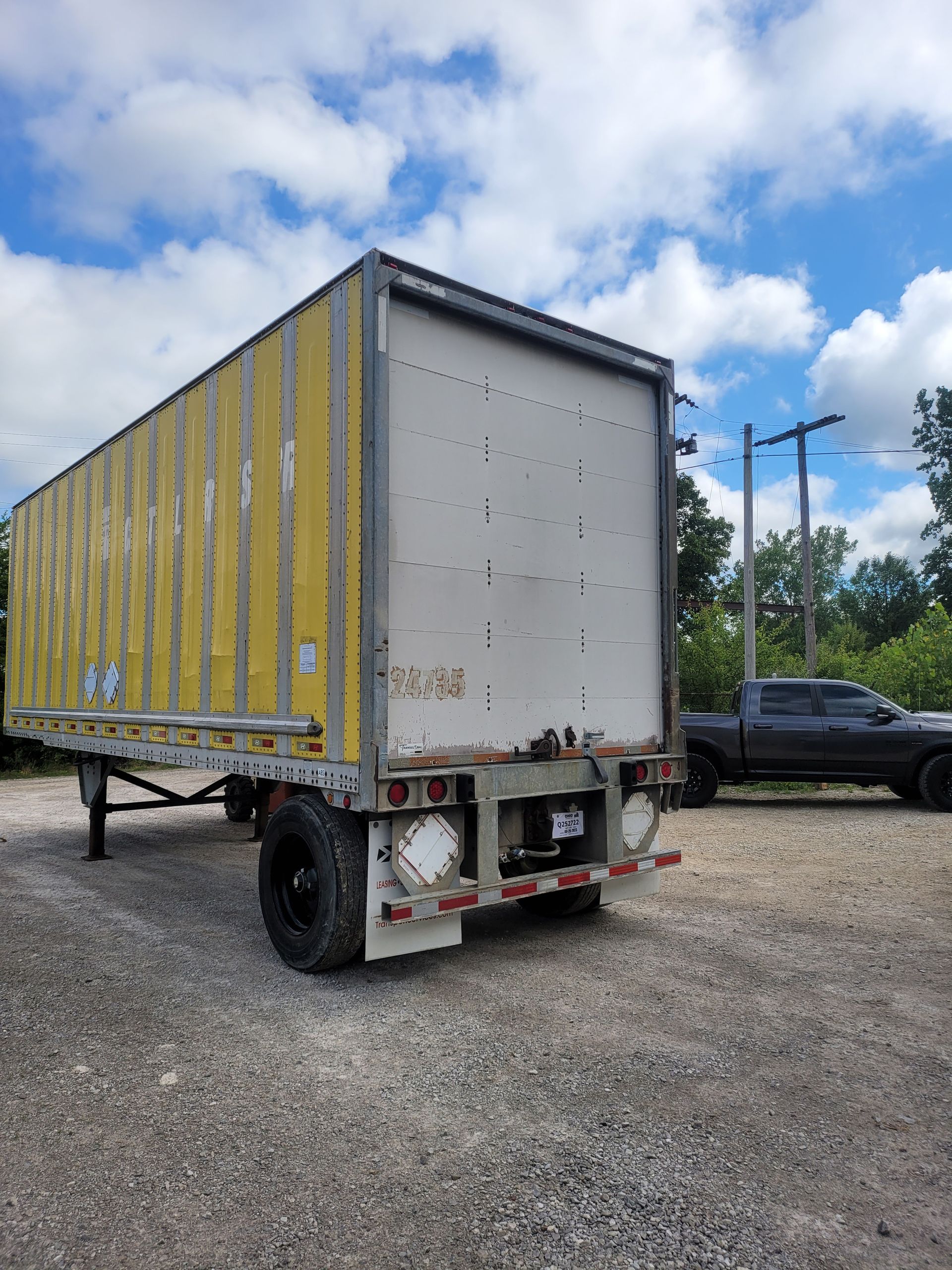 A semi truck is parked in a gravel lot next to a truck.