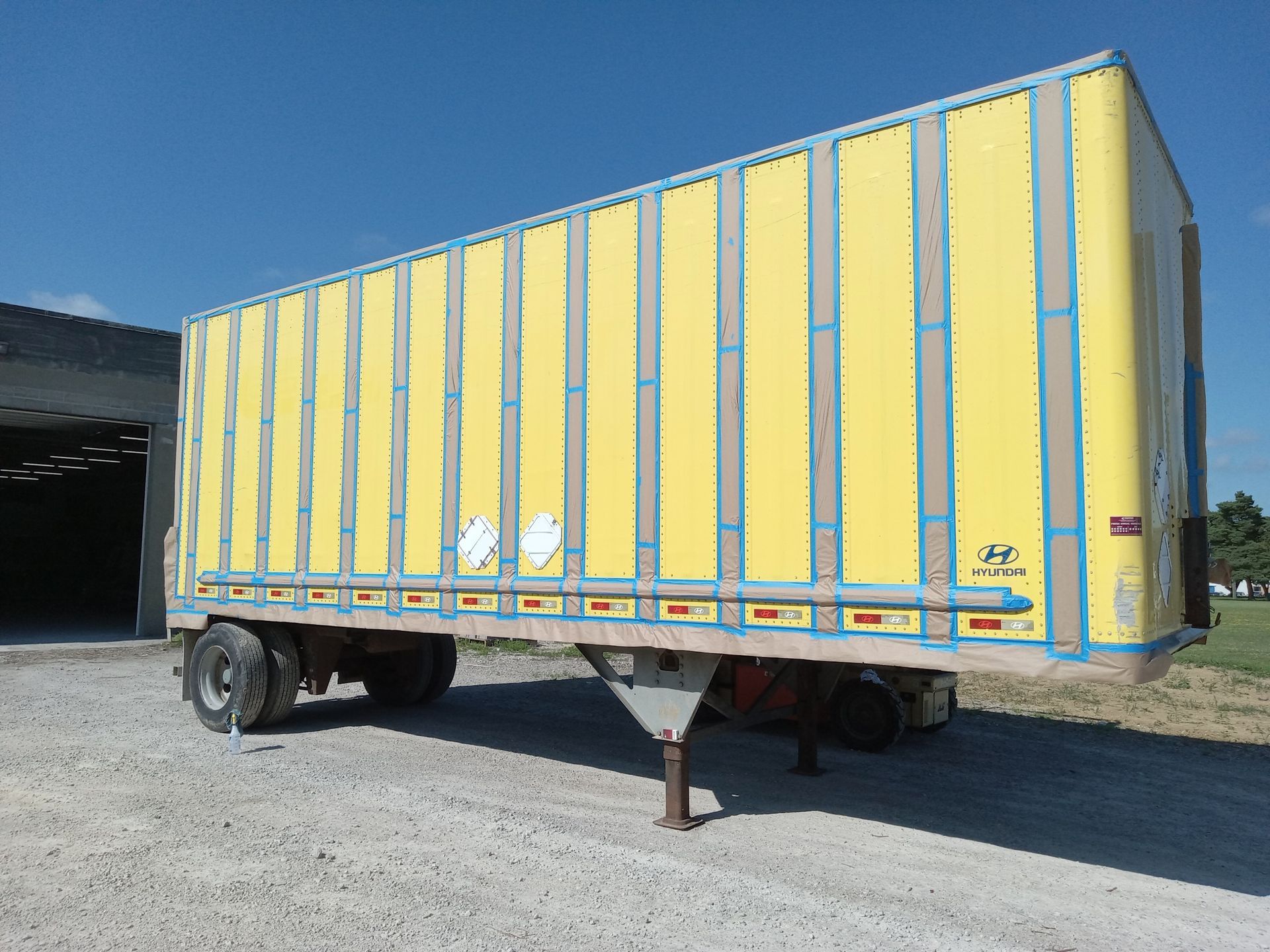 A yellow trailer is parked in a gravel lot