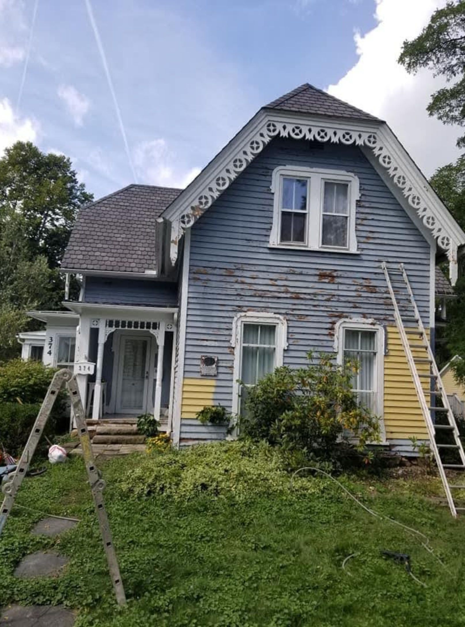 A blue and yellow house with a ladder in front of it.
