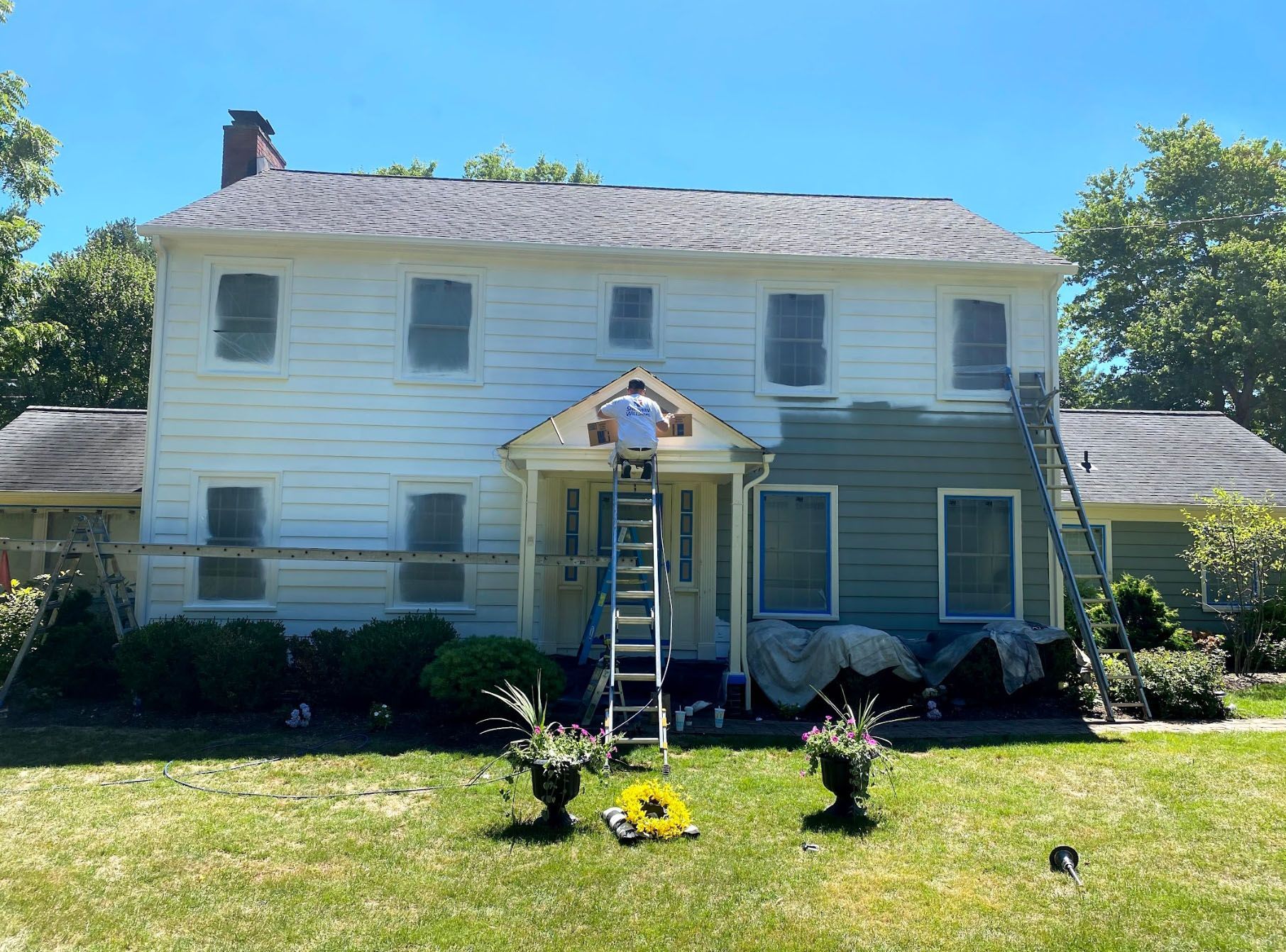 A man is standing on a ladder painting the side of a house.