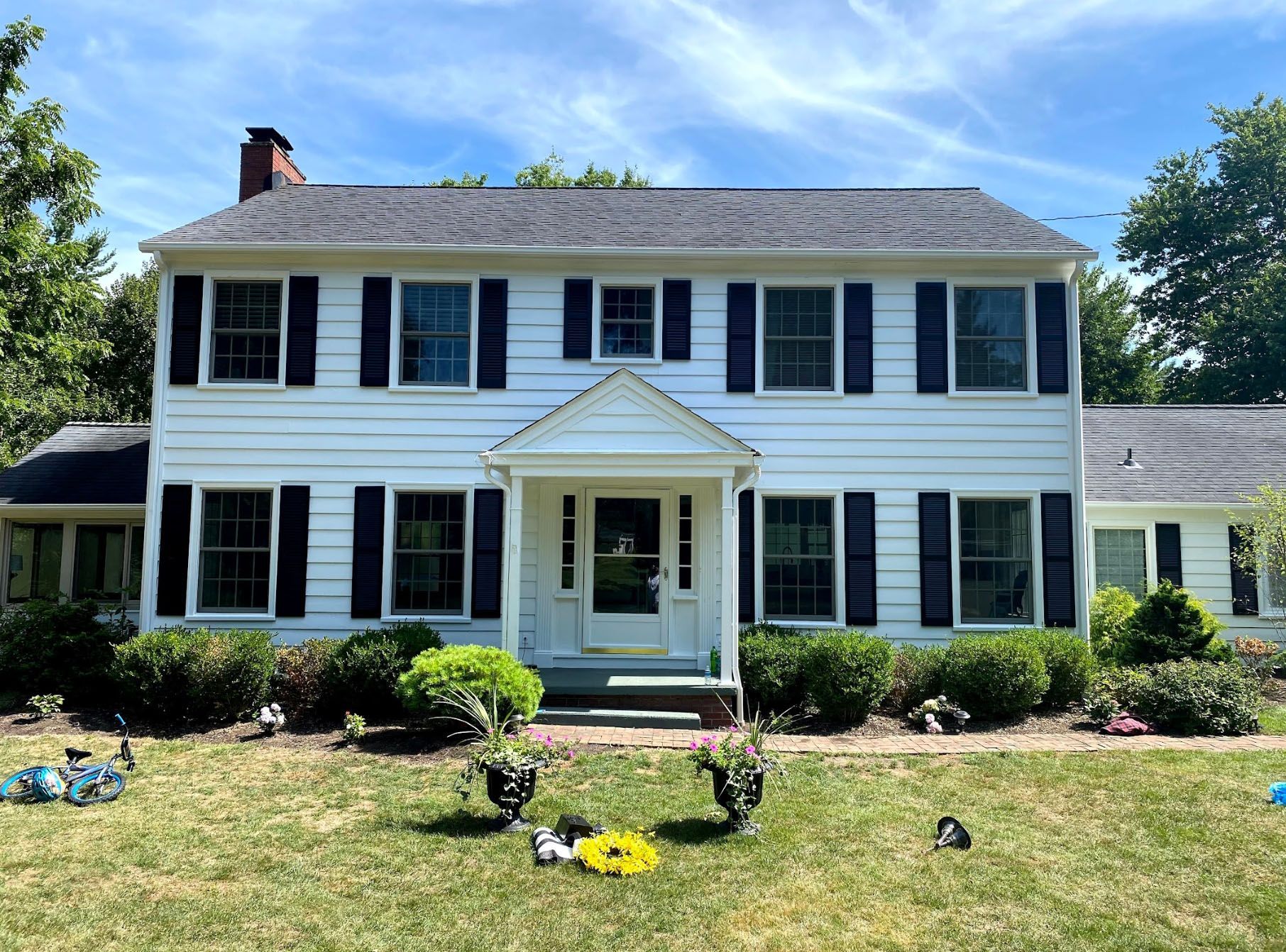 A large white house with black shutters is sitting on top of a lush green lawn.