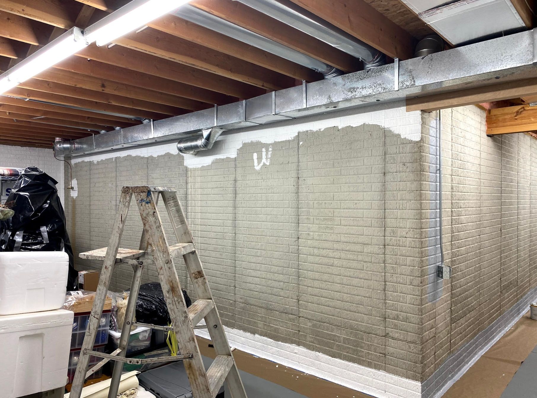 A ladder is sitting in a basement next to a brick wall.