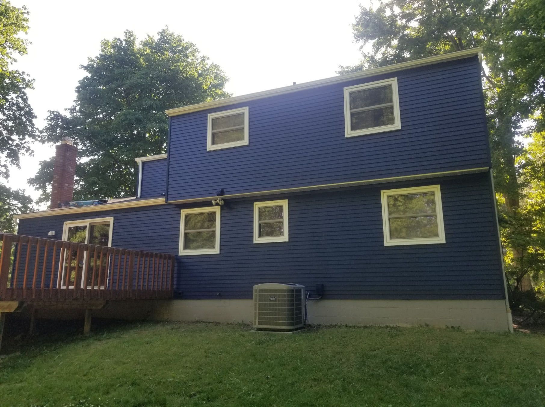 The back of a blue house with a deck and air conditioner.