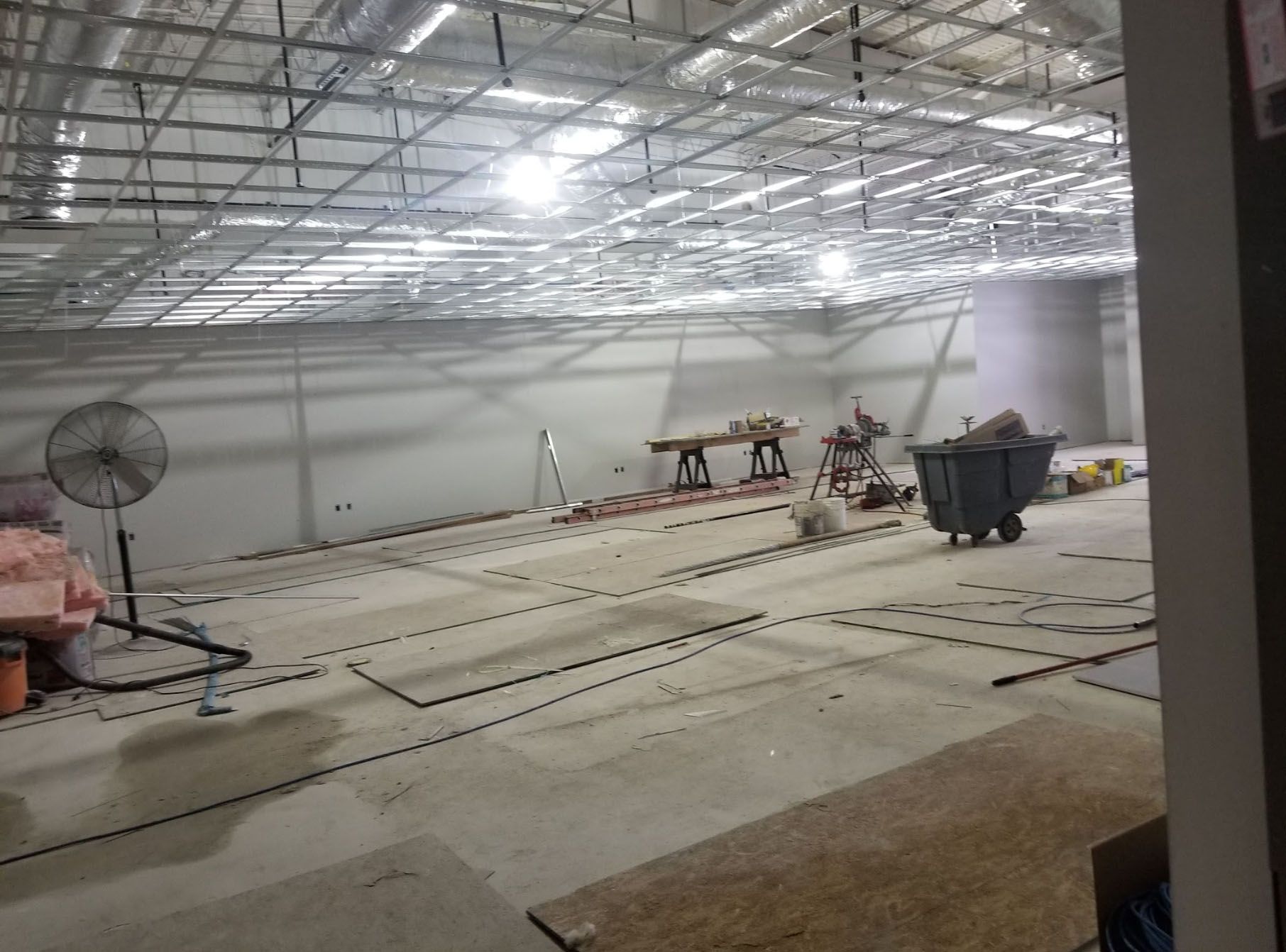 A large empty room with a fan and a trash can in it.