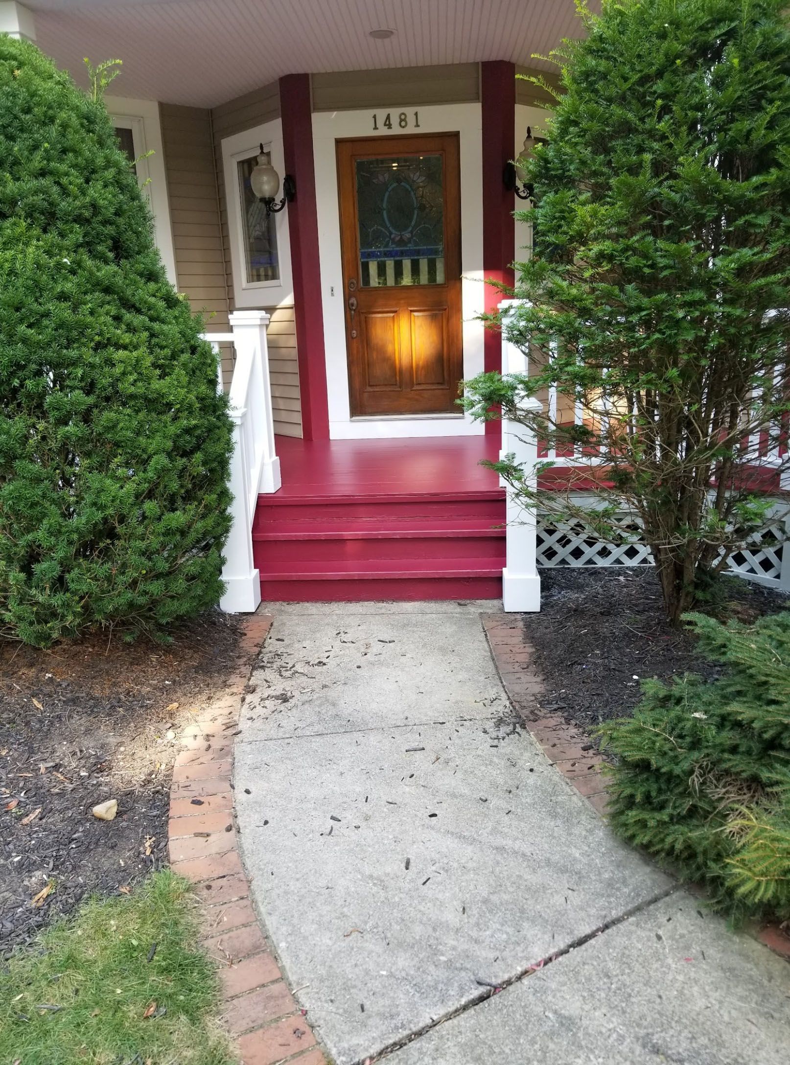 The front porch of a house with red steps and a walkway leading to it.