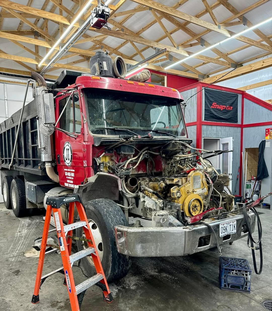 A red dump truck is being worked on in a garage.