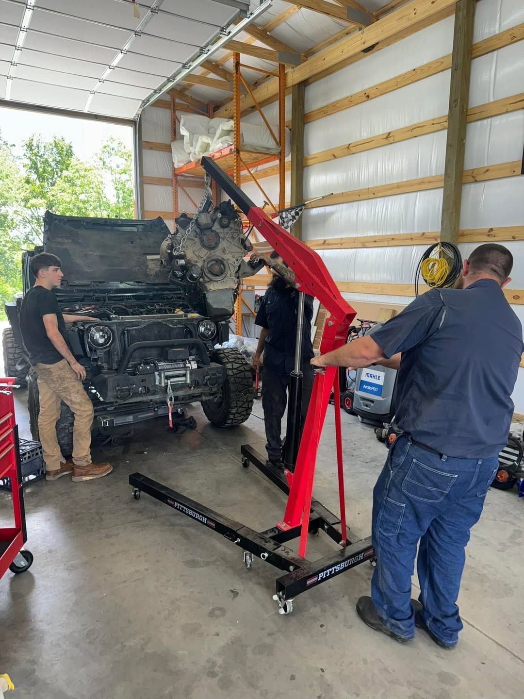 A group of men are working on a jeep engine in a garage.
