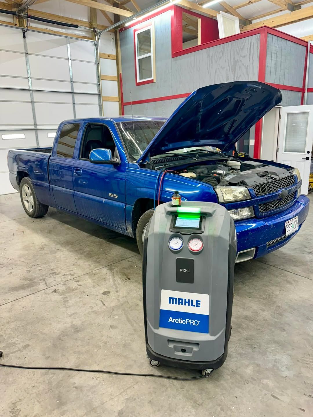 A blue truck with the hood up is sitting in a garage next to a machine.