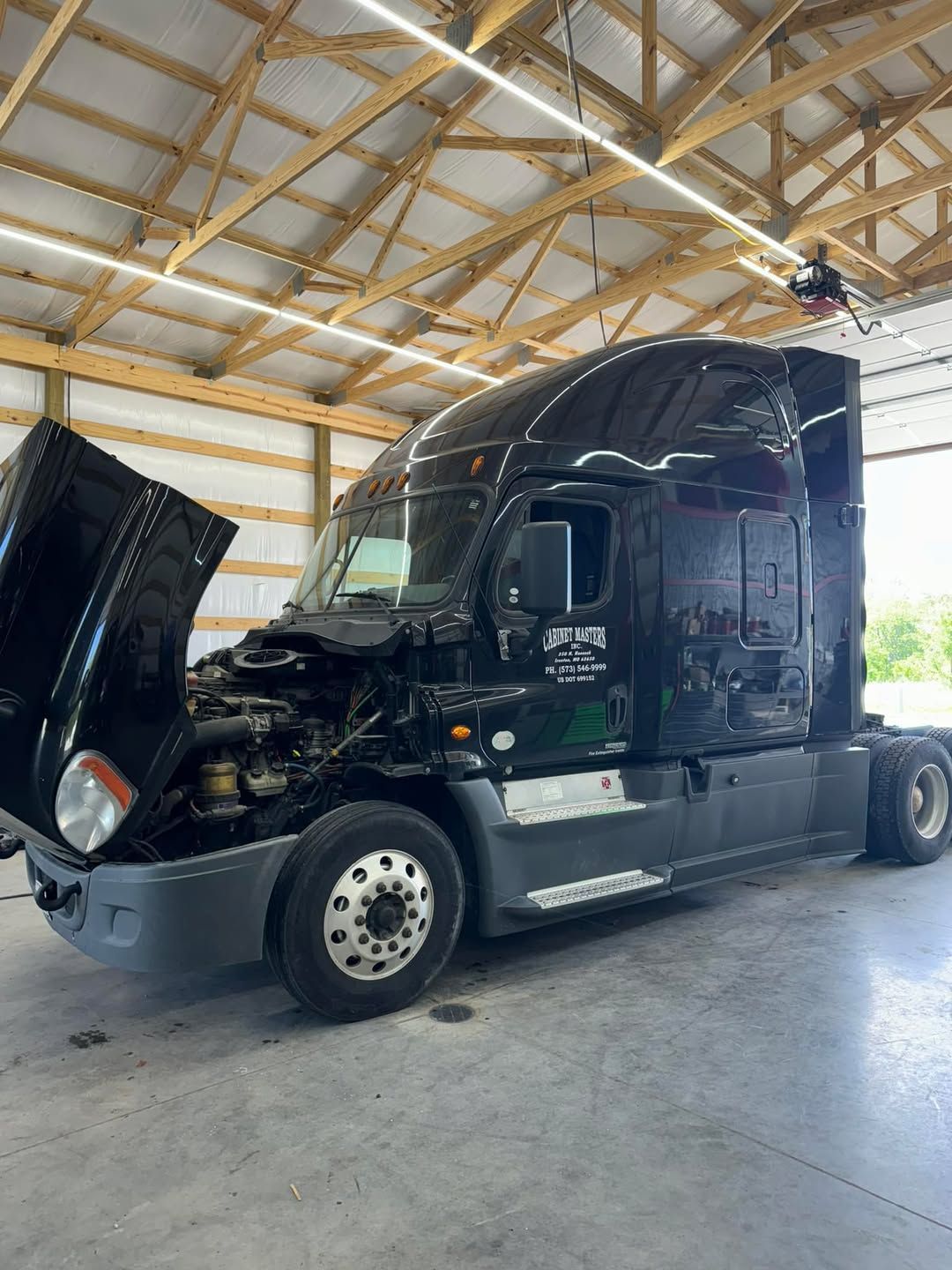 A black semi truck with its hood open is parked in a garage.